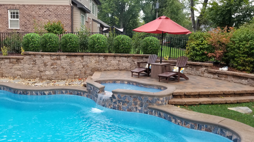 This is an example of a large traditional backyard custom-shaped pool in St Louis with stamped concrete.