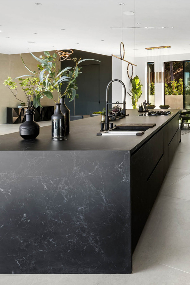 Photo of an expansive modern u-shaped kitchen in Los Angeles with a double-bowl sink, flat-panel cabinets, black cabinets, solid surface benchtops, black splashback, porcelain splashback, black appliances, with island, grey floor and black benchtop.