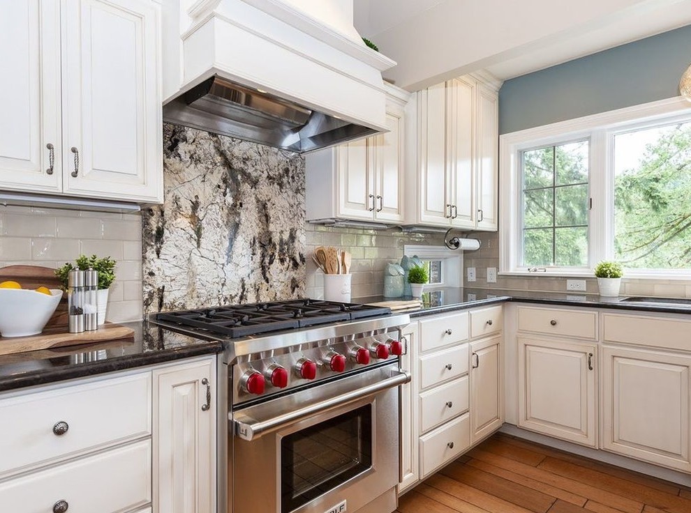 Photo of a large traditional kitchen in Portland with an undermount sink, raised-panel cabinets, white cabinets, granite benchtops, white splashback, subway tile splashback, stainless steel appliances, medium hardwood floors, with island, brown floor and brown benchtop.