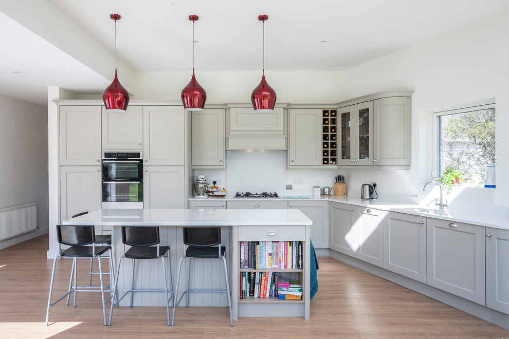 Photo of a large contemporary l-shaped open plan kitchen in Dublin with grey cabinets, quartzite benchtops, white splashback, with island, white benchtop, an undermount sink, shaker cabinets, light hardwood floors and brown floor.