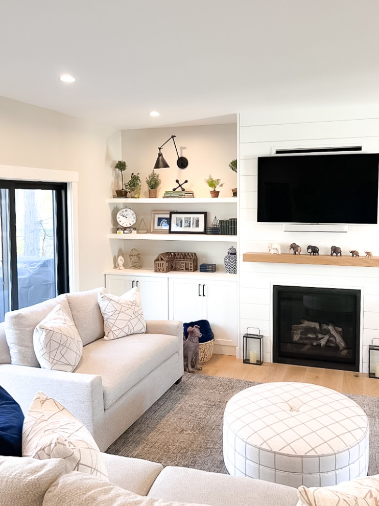 Photo of a large country open concept family room in Portland Maine with beige walls, light hardwood floors, a standard fireplace and a wall-mounted tv.