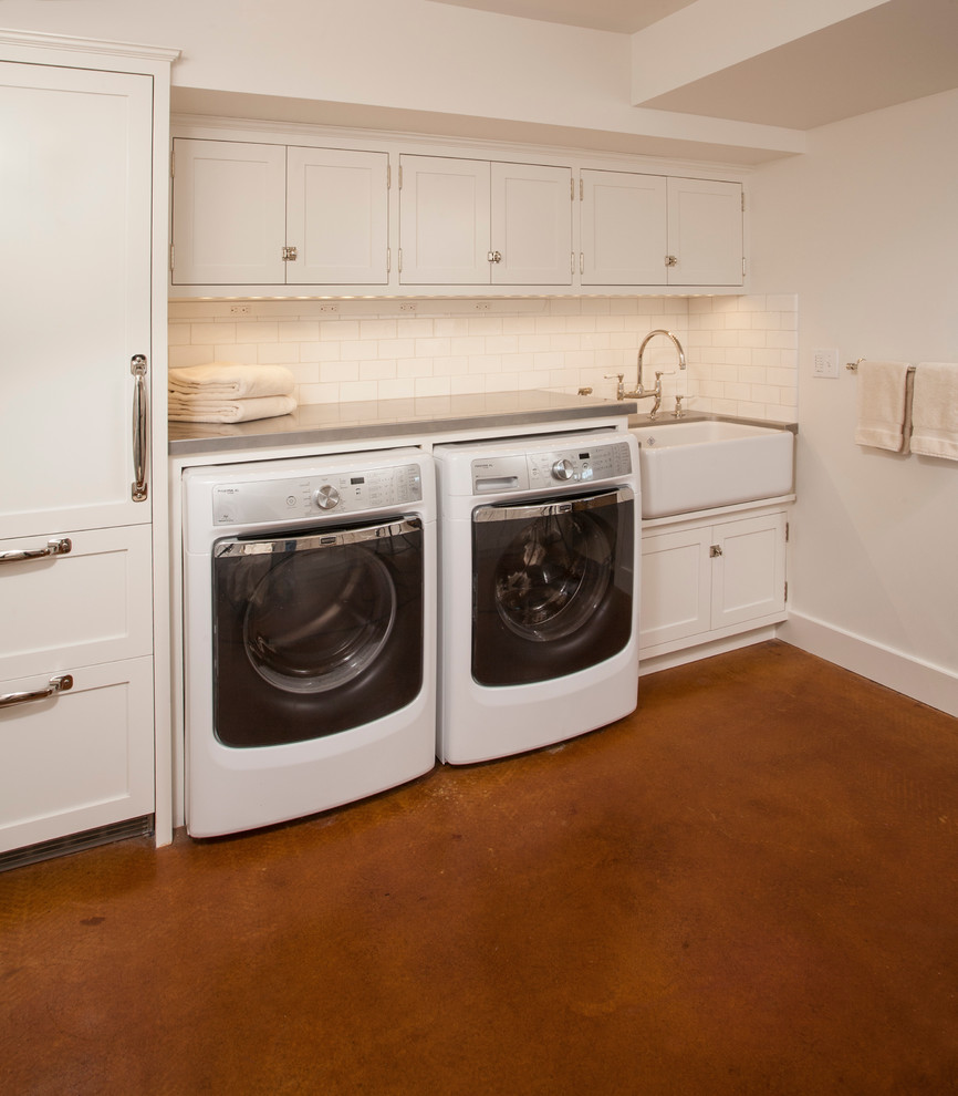 This is an example of a mid-sized transitional u-shaped dedicated laundry room in Seattle with a farmhouse sink, shaker cabinets, white cabinets, zinc benchtops, white walls, concrete floors and a side-by-side washer and dryer.