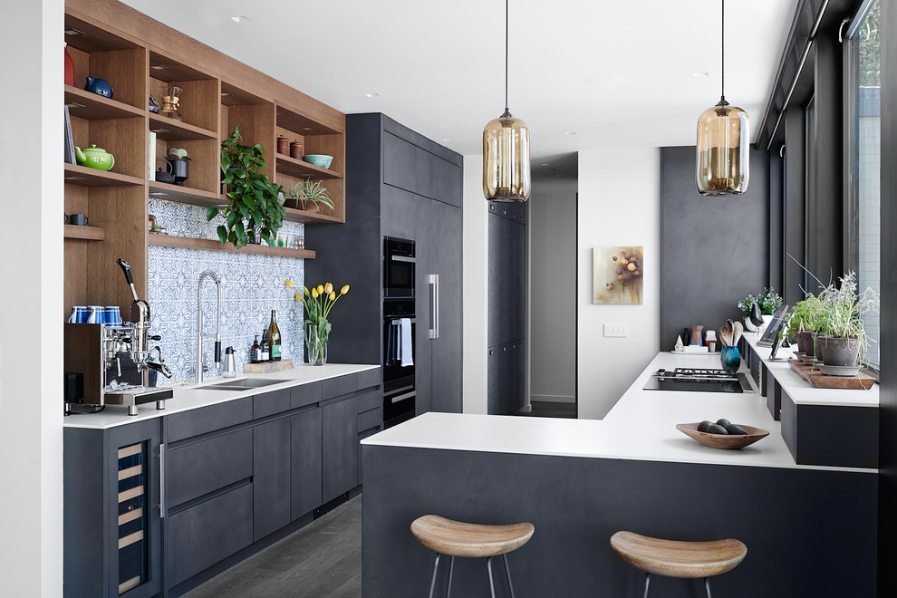 This is an example of a midcentury l-shaped kitchen in San Francisco with a double-bowl sink, flat-panel cabinets, black cabinets, multi-coloured splashback, panelled appliances, a peninsula, brown floor and white benchtop.