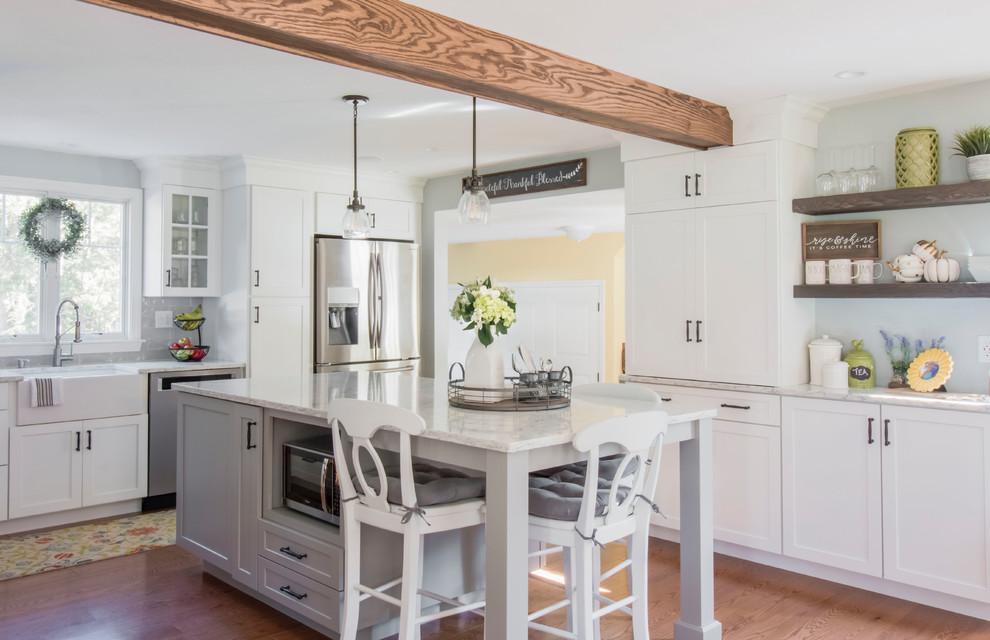 Photo of a country u-shaped kitchen in Boston with a farmhouse sink, shaker cabinets, white cabinets, grey splashback, subway tile splashback, stainless steel appliances, with island, medium hardwood floors, brown floor and white benchtop.