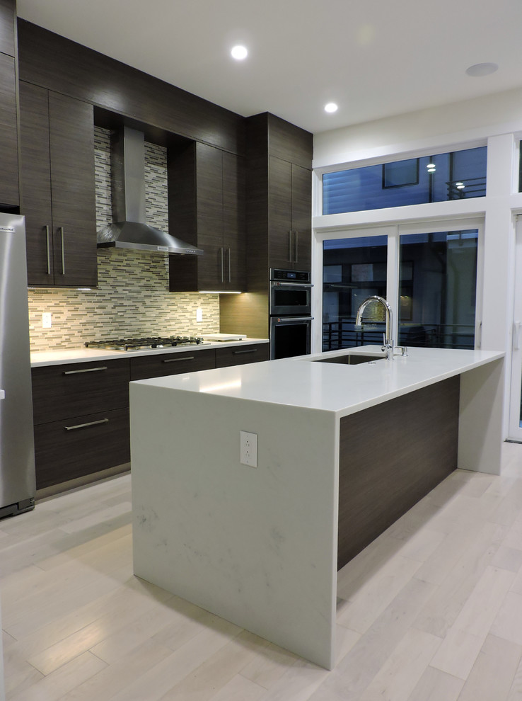This is an example of a modern eat-in kitchen in Philadelphia with a single-bowl sink, flat-panel cabinets, dark wood cabinets, quartzite benchtops, multi-coloured splashback, stainless steel appliances, light hardwood floors, with island and white benchtop.