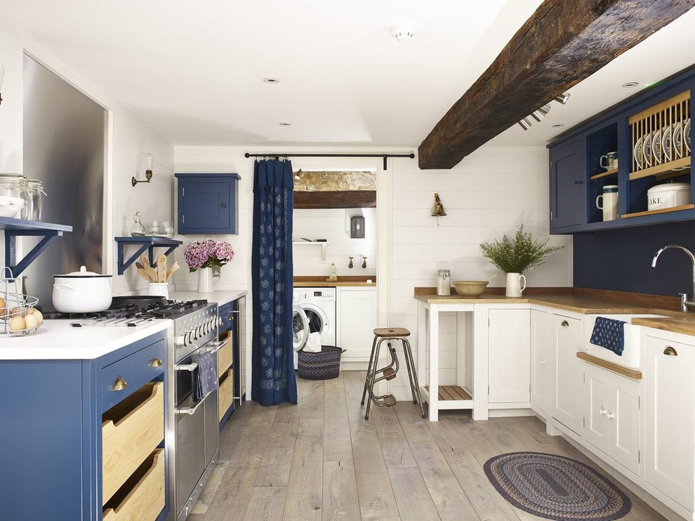 Design ideas for a beach style u-shaped separate kitchen in Wiltshire with a farmhouse sink, blue cabinets, wood benchtops, metallic splashback, stainless steel appliances, medium hardwood floors, no island and beige floor.