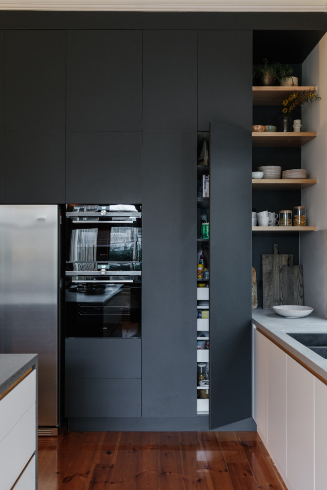 Photo of a mid-sized midcentury l-shaped eat-in kitchen in Adelaide with an undermount sink, flat-panel cabinets, black cabinets, solid surface benchtops, grey splashback, stone slab splashback, panelled appliances, light hardwood floors, with island, brown floor and grey benchtop.