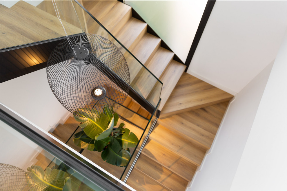На фото: большая п-образная деревянная лестница в стиле модернизм с деревянными ступенями и стеклянными перилами с