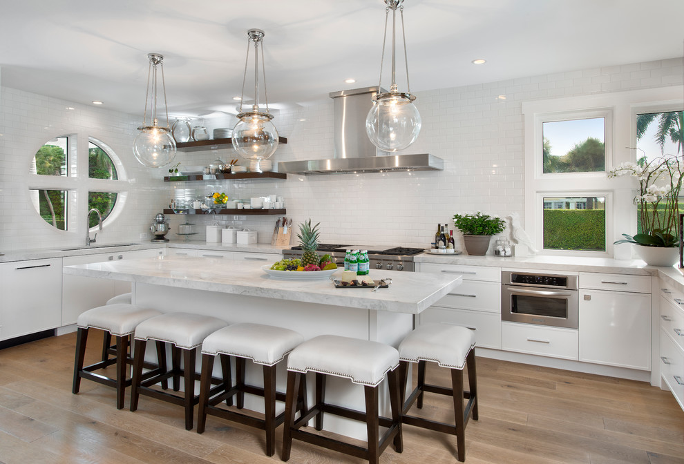 Design ideas for a contemporary l-shaped kitchen in Miami with flat-panel cabinets, white cabinets, white splashback, subway tile splashback, stainless steel appliances, medium hardwood floors, with island, brown floor and white benchtop.