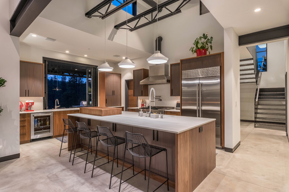 Inspiration for a contemporary l-shaped concrete floor and gray floor kitchen remodel in San Francisco with an undermount sink, flat-panel cabinets, medium tone wood cabinets, white backsplash, stainless steel appliances, an island and white countertops