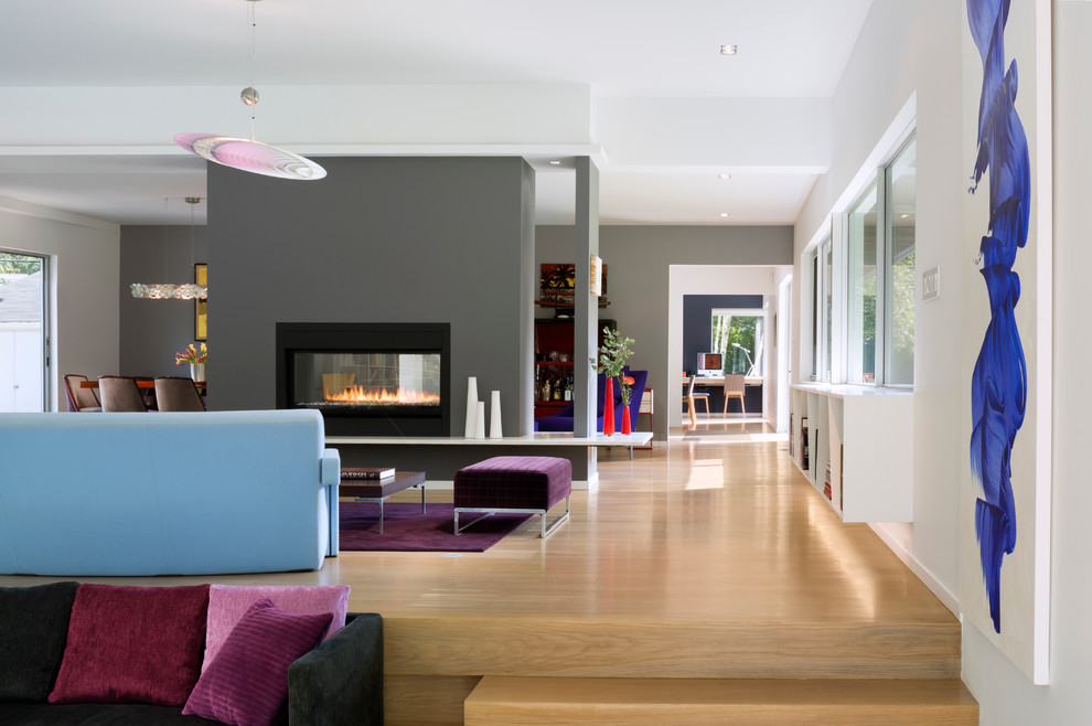 This is an example of a large contemporary open concept living room in San Francisco with white walls, medium hardwood floors, a two-sided fireplace, a metal fireplace surround, a wall-mounted tv and brown floor.