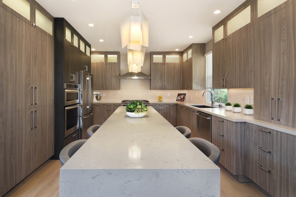 Mid-sized contemporary u-shaped eat-in kitchen in Orange County with an undermount sink, flat-panel cabinets, quartz benchtops, porcelain splashback, stainless steel appliances, light hardwood floors, with island, beige floor, white benchtop, medium wood cabinets and beige splashback.
