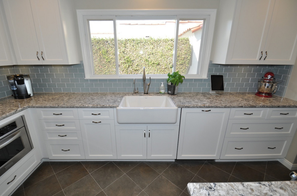 Photo of a mid-sized traditional l-shaped separate kitchen in Los Angeles with a farmhouse sink, shaker cabinets, white cabinets, blue splashback, glass tile splashback, stainless steel appliances, porcelain floors and no island.