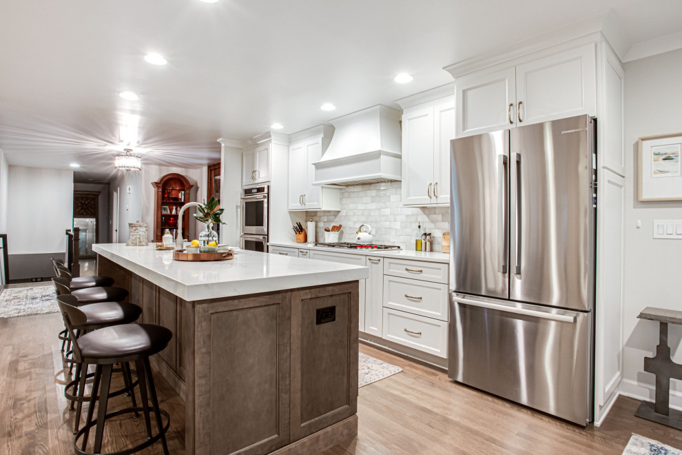 Mid-sized transitional single-wall eat-in kitchen in Atlanta with an undermount sink, shaker cabinets, white cabinets, quartz benchtops, white splashback, subway tile splashback, stainless steel appliances, medium hardwood floors, with island, brown floor and white benchtop.