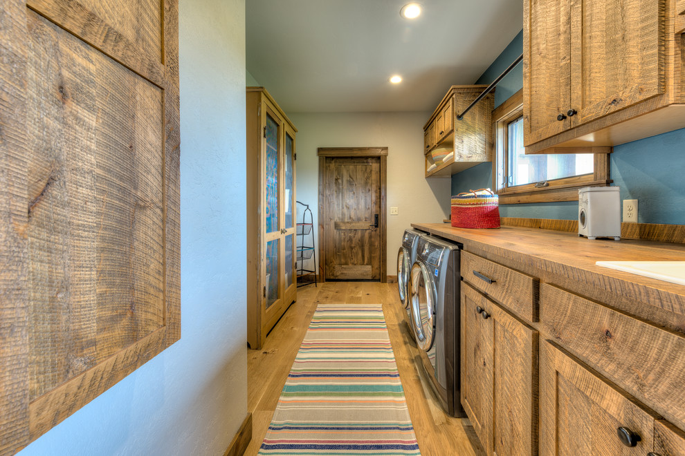 Photo of a country galley dedicated laundry room in Other with a drop-in sink, shaker cabinets, medium wood cabinets, wood benchtops, medium hardwood floors, a side-by-side washer and dryer, brown floor, brown benchtop and grey walls.