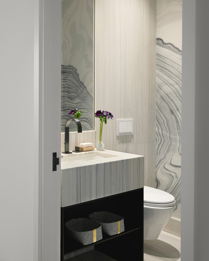 Small contemporary cloakroom in New York with open cabinets, dark wood cabinets, a wall mounted toilet, beige tiles, stone tiles, grey walls, ceramic flooring, a submerged sink, marble worktops, beige floors, grey worktops, a built in vanity unit and wallpapered walls.