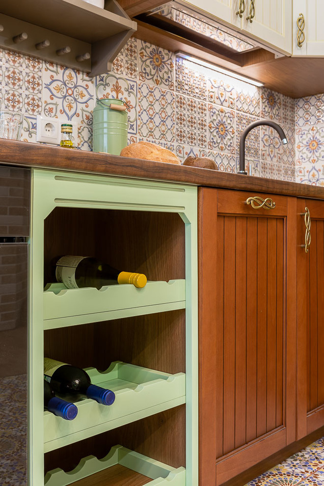 This is an example of a mid-sized traditional l-shaped separate kitchen in Novosibirsk with a farmhouse sink, green cabinets, laminate benchtops, beige splashback, ceramic splashback, stainless steel appliances, ceramic floors, no island, beige floor and brown benchtop.