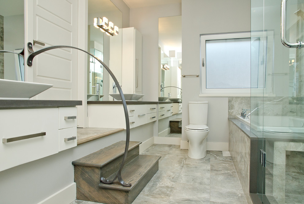 Inspiration for a beach style bathroom in Toronto with a vessel sink, flat-panel cabinets, white cabinets, a drop-in tub, a corner shower, a two-piece toilet and gray tile.