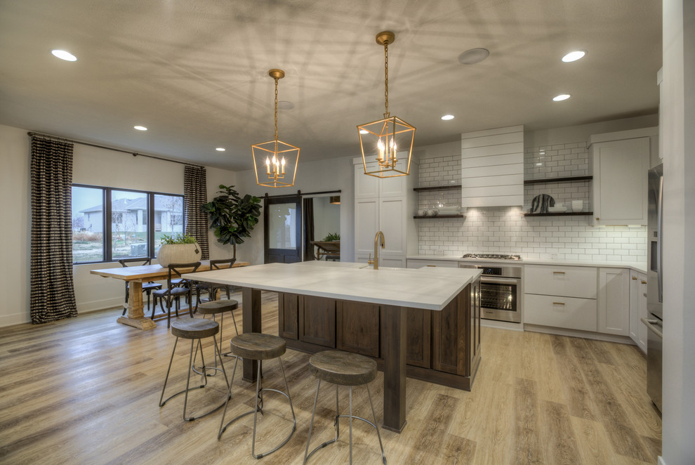 This is an example of a country l-shaped eat-in kitchen in Omaha with a farmhouse sink, shaker cabinets, dark wood cabinets, white splashback, subway tile splashback, stainless steel appliances, light hardwood floors, with island, beige floor and grey benchtop.