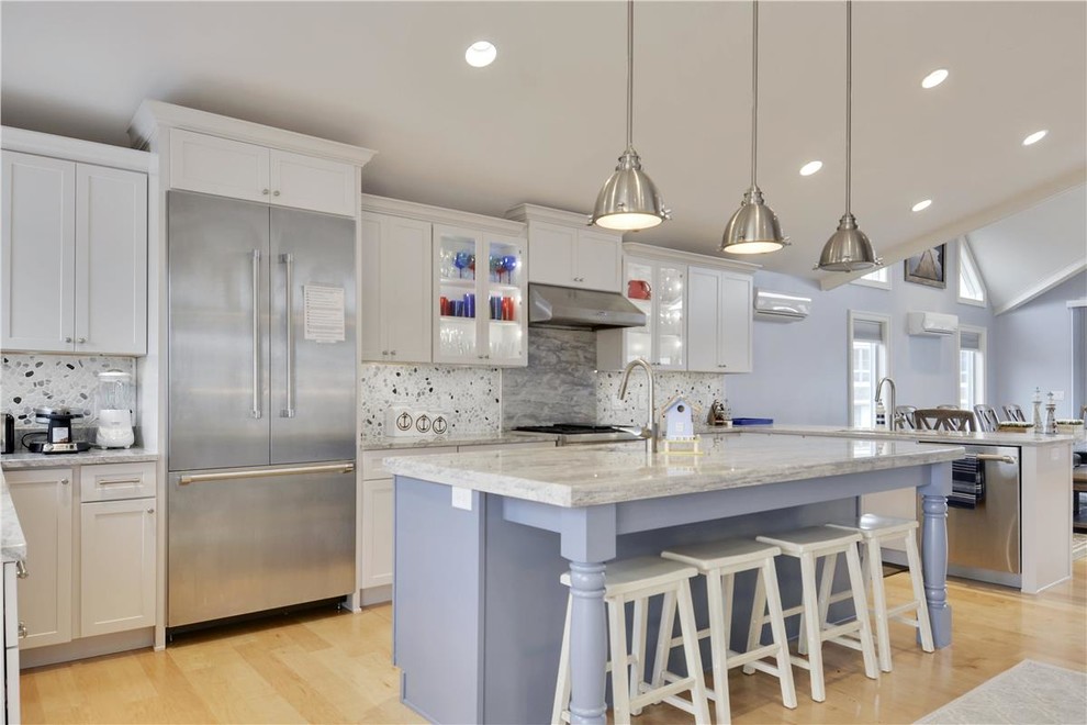 Inspiration for a mid-sized beach style u-shaped eat-in kitchen in Other with an undermount sink, recessed-panel cabinets, white cabinets, solid surface benchtops, white splashback, ceramic splashback, stainless steel appliances, light hardwood floors and with island.