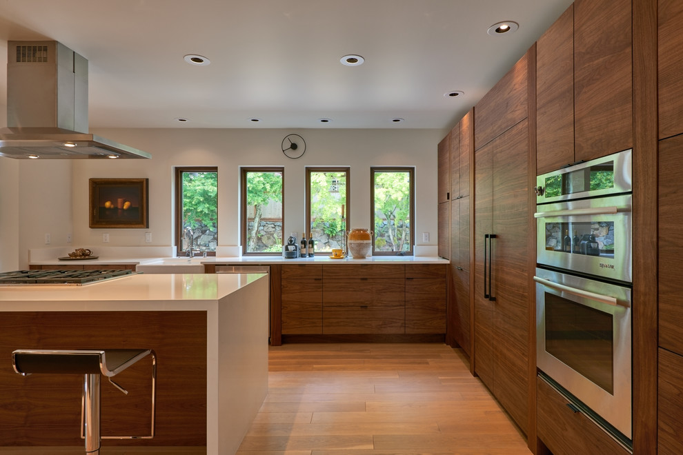 Inspiration for a mid-sized midcentury l-shaped eat-in kitchen in Seattle with a farmhouse sink, flat-panel cabinets, medium wood cabinets, quartz benchtops, white splashback, stainless steel appliances, light hardwood floors and with island.