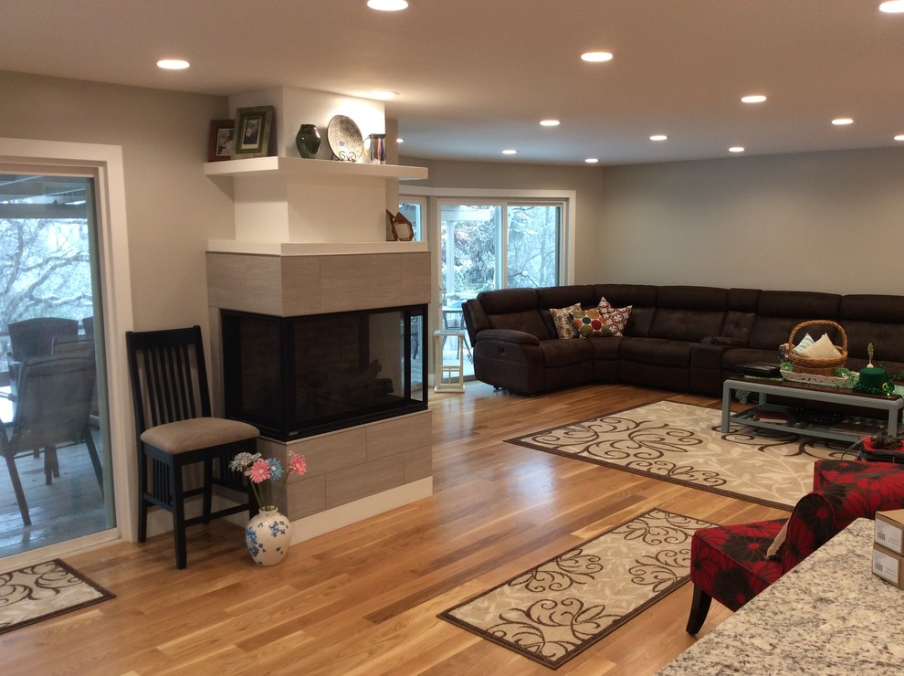 Photo of a large transitional open concept living room in Salt Lake City with beige walls, light hardwood floors, a two-sided fireplace, a tile fireplace surround, a wall-mounted tv and beige floor.