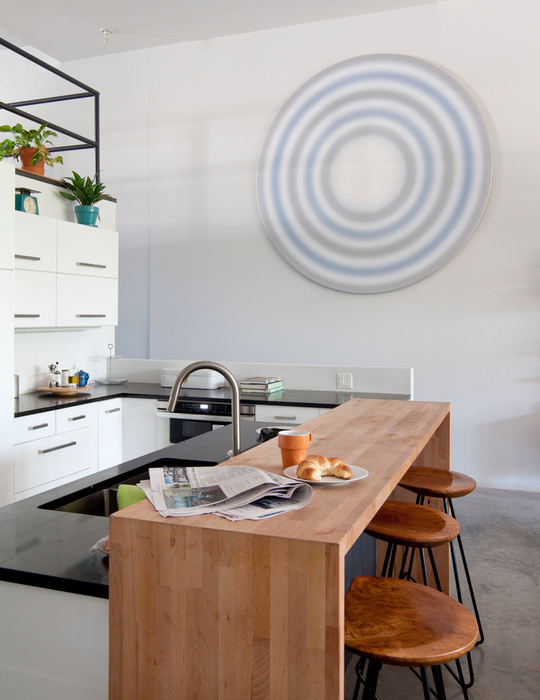 Trendy u-shaped eat-in kitchen photo in New York with flat-panel cabinets, white cabinets, white backsplash, subway tile backsplash, stainless steel appliances and an island