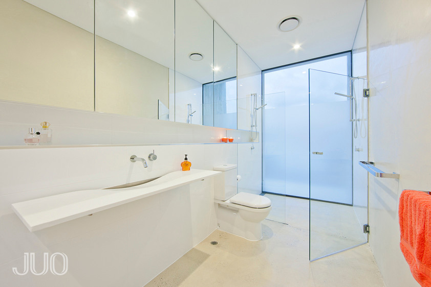 Inspiration for a large modern master bathroom in Perth with a wall-mount sink, flat-panel cabinets, white cabinets, solid surface benchtops, a double shower, a one-piece toilet, white tile, ceramic tile, white walls and concrete floors.