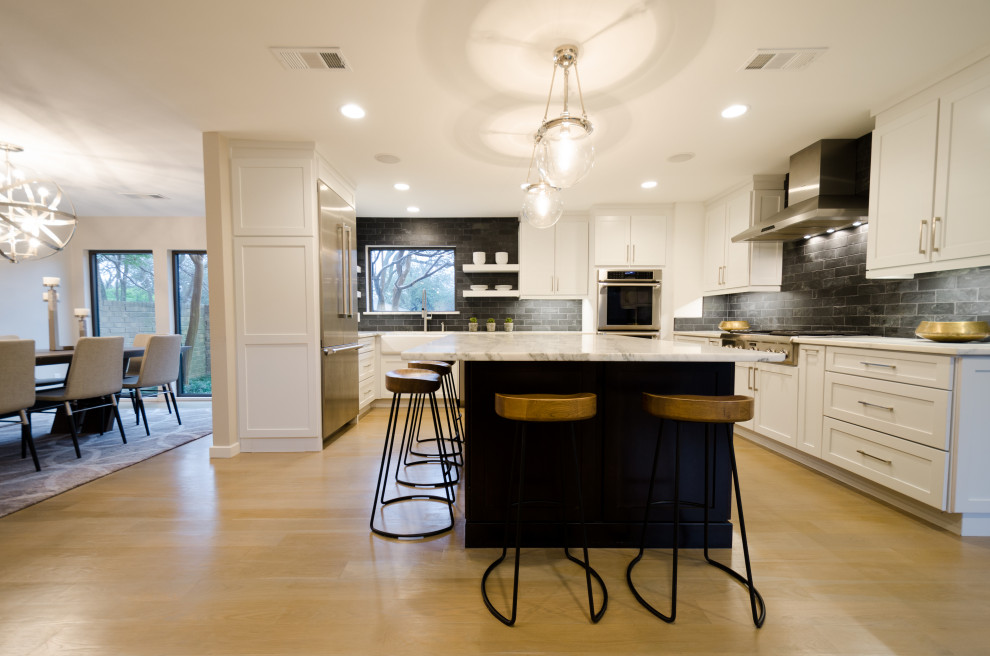 This is an example of a large country u-shaped eat-in kitchen in Portland with a farmhouse sink, shaker cabinets, white cabinets, marble benchtops, black splashback, marble splashback, stainless steel appliances, light hardwood floors, with island, beige floor and white benchtop.
