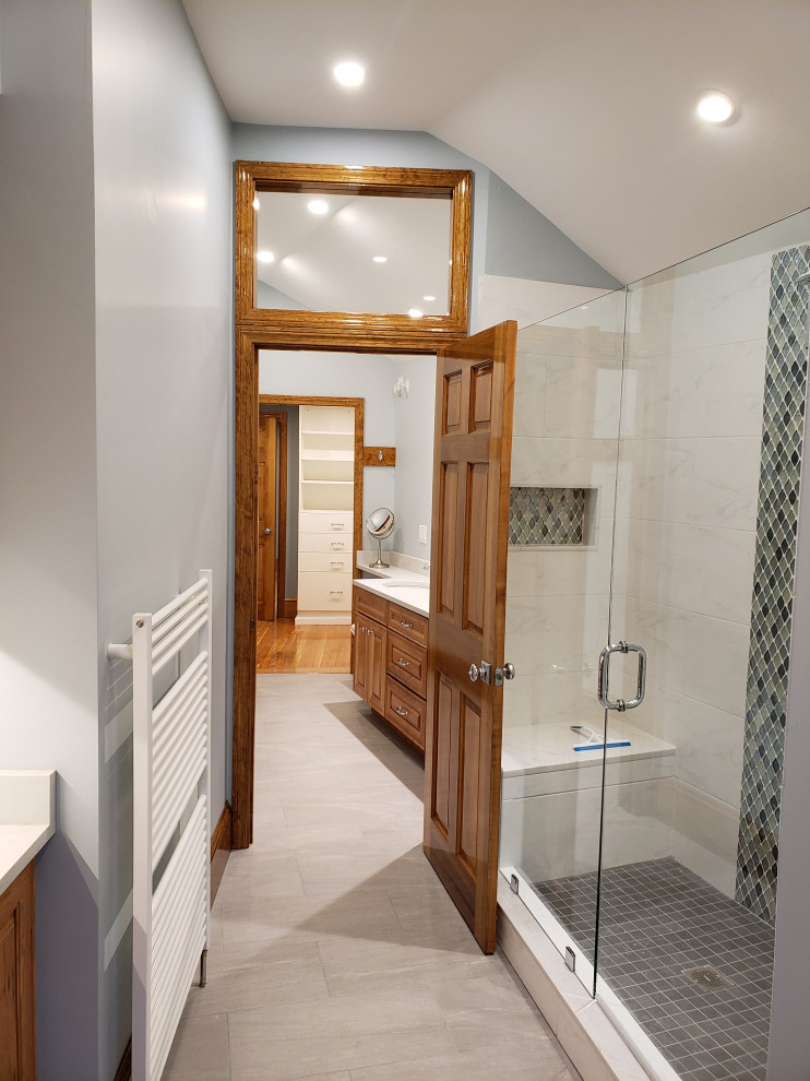 Photo of a mid-sized contemporary master bathroom in Boston with raised-panel cabinets, medium wood cabinets, an alcove shower, a bidet, white tile, marble, blue walls, ceramic floors, an undermount sink, engineered quartz benchtops, grey floor, a hinged shower door, white benchtops, a laundry, a double vanity, a built-in vanity and vaulted.