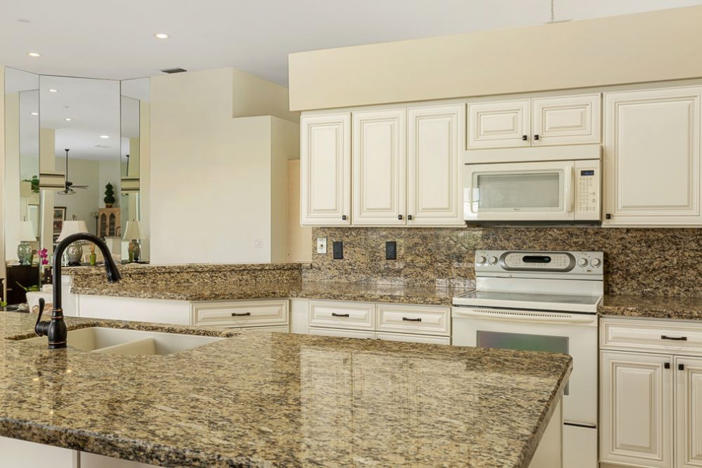 Design ideas for a mid-sized traditional l-shaped eat-in kitchen in Miami with a drop-in sink, raised-panel cabinets, beige cabinets, granite benchtops, yellow splashback, granite splashback, white appliances, ceramic floors, with island and yellow benchtop.