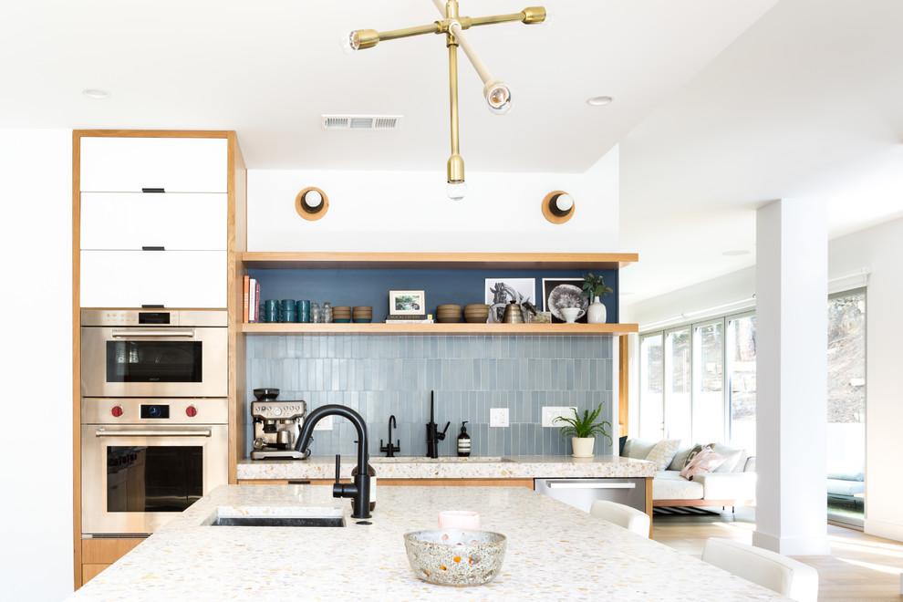 Large midcentury galley open plan kitchen in Los Angeles with an undermount sink, flat-panel cabinets, blue cabinets, concrete benchtops, blue splashback, ceramic splashback, stainless steel appliances, light hardwood floors and with island.