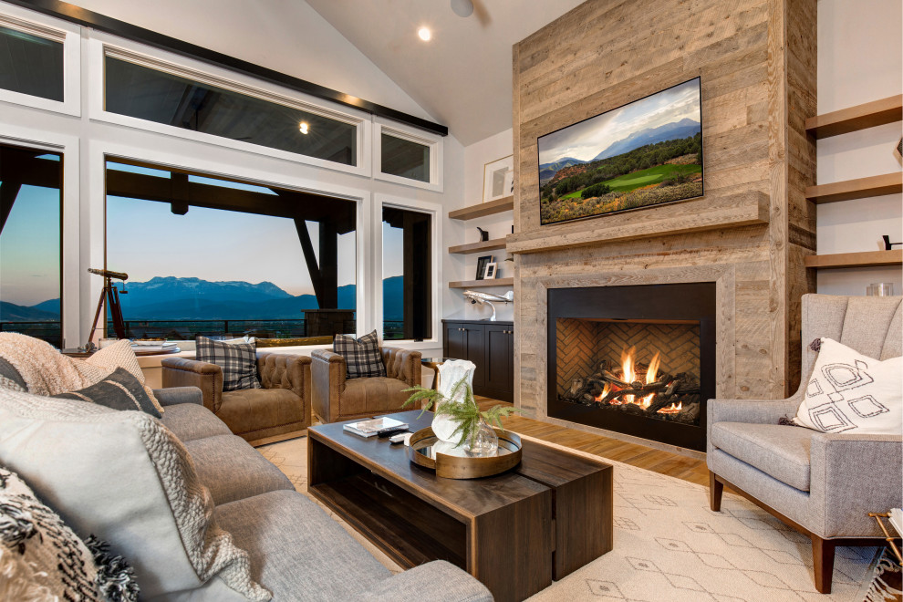 This is an example of a country family room in Salt Lake City with grey walls, medium hardwood floors, a ribbon fireplace, a wood fireplace surround, a wall-mounted tv and vaulted.