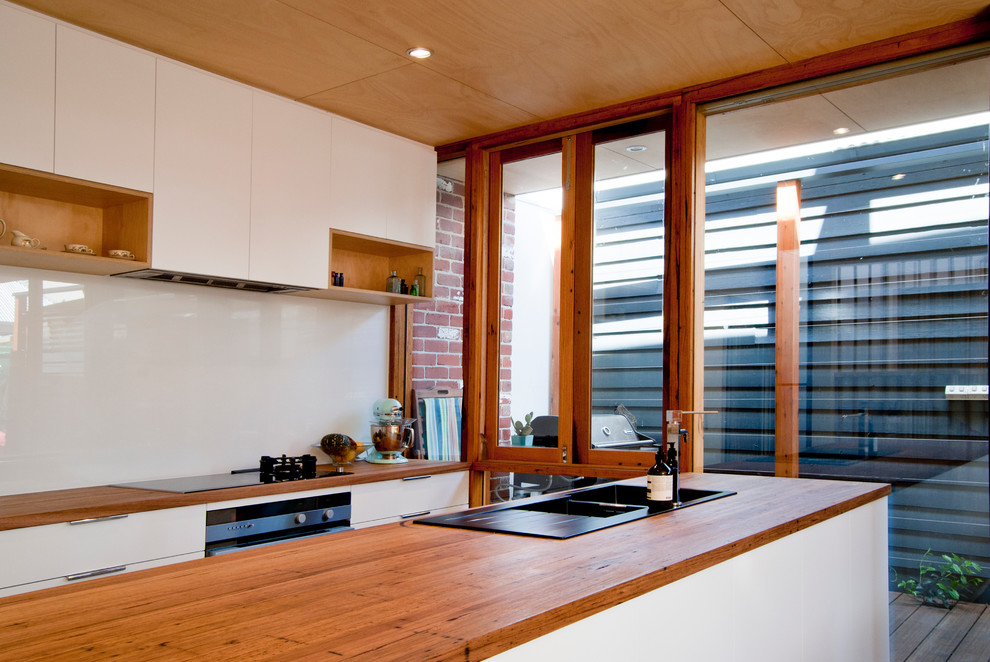 This is an example of a contemporary kitchen in Melbourne with flat-panel cabinets, white cabinets, white splashback, concrete floors and with island.