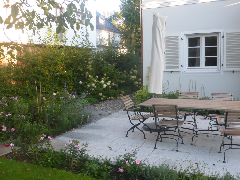 Patio im Sommer and neben dem Haus With Blumenbeet, direkter Sonneneinstrahlung and Natursteinplatten in Munich