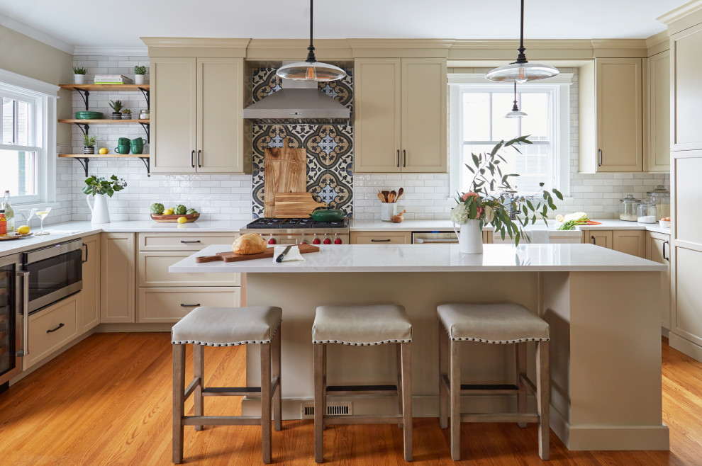 Photo of a traditional u-shaped eat-in kitchen in Chicago with a farmhouse sink, shaker cabinets, beige cabinets, quartzite benchtops, multi-coloured splashback, porcelain splashback, stainless steel appliances, medium hardwood floors, with island and beige benchtop.