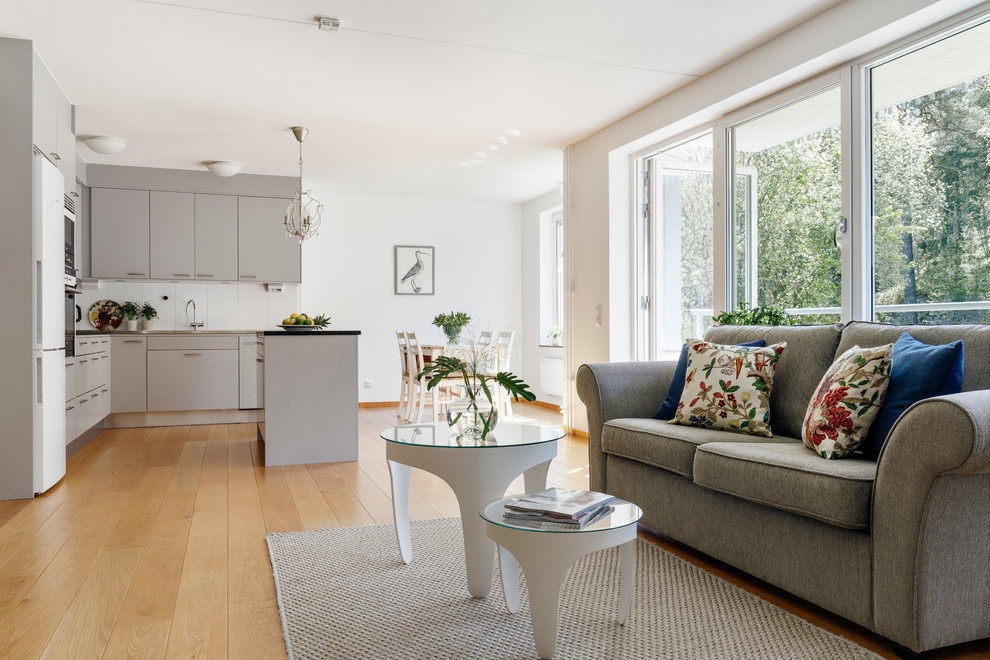 This is an example of a mid-sized contemporary open concept living room in Stockholm with white walls, light hardwood floors, no fireplace and no tv.