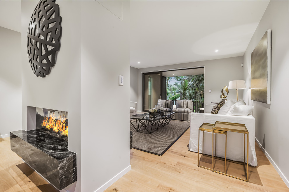 Inspiration for a mid-sized contemporary open concept living room in Auckland with white walls, light hardwood floors, a two-sided fireplace, a plaster fireplace surround and a wall-mounted tv.