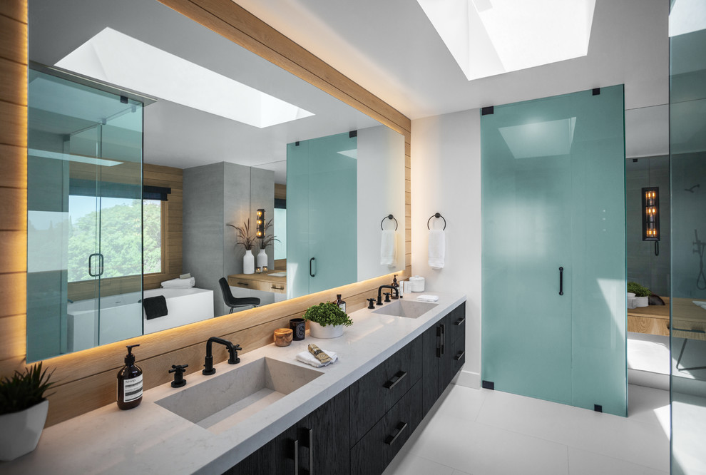 This is an example of a large contemporary master bathroom in Los Angeles with flat-panel cabinets, black cabinets, gray tile, white walls, vinyl floors, marble benchtops, white floor, grey benchtops, an integrated sink, a freestanding tub, a corner shower, a one-piece toilet, a hinged shower door and cement tile.