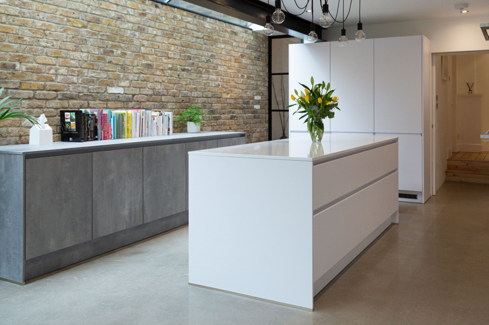 Inspiration for a mid-sized contemporary galley open plan kitchen in London with an undermount sink, flat-panel cabinets, white cabinets, solid surface benchtops, grey splashback, porcelain splashback, black appliances, concrete floors, with island, grey floor and grey benchtop.