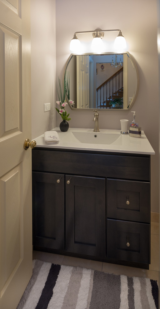 Photo of a small transitional powder room in Chicago with shaker cabinets, dark wood cabinets, a two-piece toilet, marble floors, an undermount sink, engineered quartz benchtops, beige floor and white benchtops.