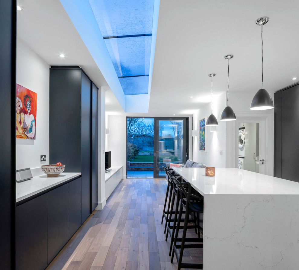 Inspiration for a contemporary kitchen in Dublin with flat-panel cabinets, black cabinets, quartzite benchtops, with island, white benchtop, dark hardwood floors and brown floor.