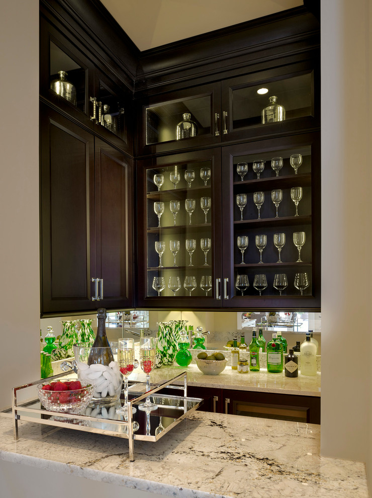 Inspiration for a transitional u-shaped home bar in Miami with recessed-panel cabinets, dark wood cabinets and mirror splashback.