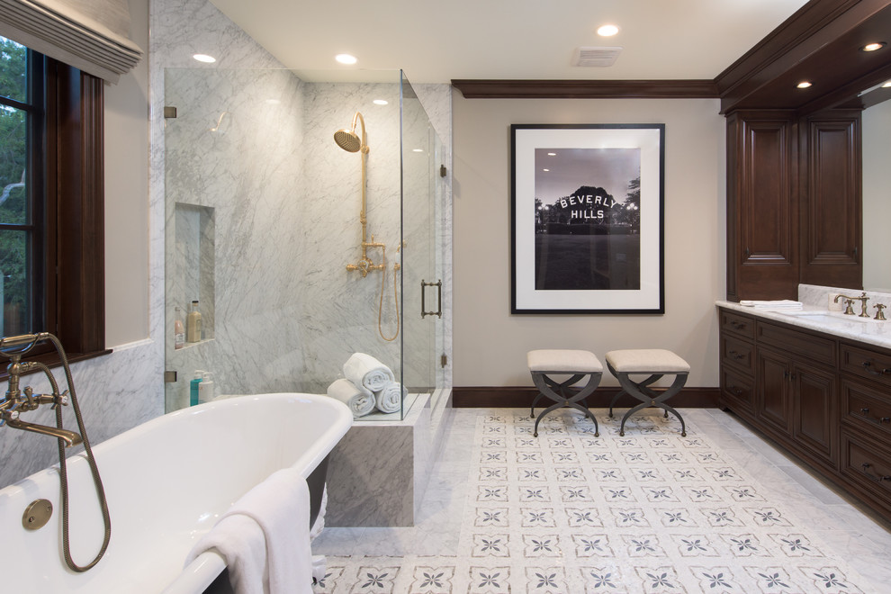 This is an example of a mediterranean master bathroom in Los Angeles with recessed-panel cabinets, dark wood cabinets, a claw-foot tub, a corner shower, gray tile, white tile, beige walls, porcelain floors, an undermount sink, marble benchtops, grey floor, a hinged shower door and white benchtops.