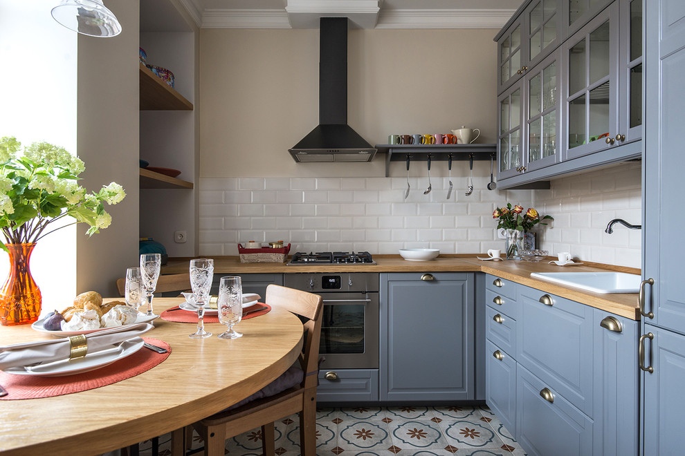 Inspiration for a small traditional l-shaped eat-in kitchen in Moscow with a drop-in sink, raised-panel cabinets, wood benchtops, white splashback, stainless steel appliances, no island, blue cabinets and ceramic splashback.