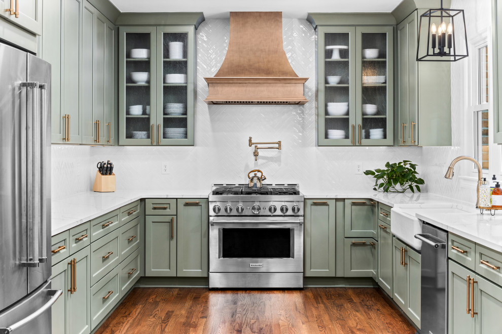 Design ideas for a transitional u-shaped kitchen in Atlanta with a farmhouse sink, shaker cabinets, green cabinets, white splashback, stainless steel appliances, dark hardwood floors, no island, brown floor and white benchtop.