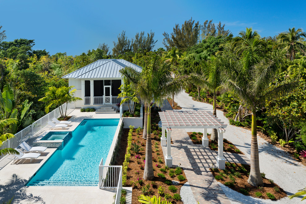 Large tropical front yard rectangular lap pool in Miami with a hot tub and natural stone pavers.