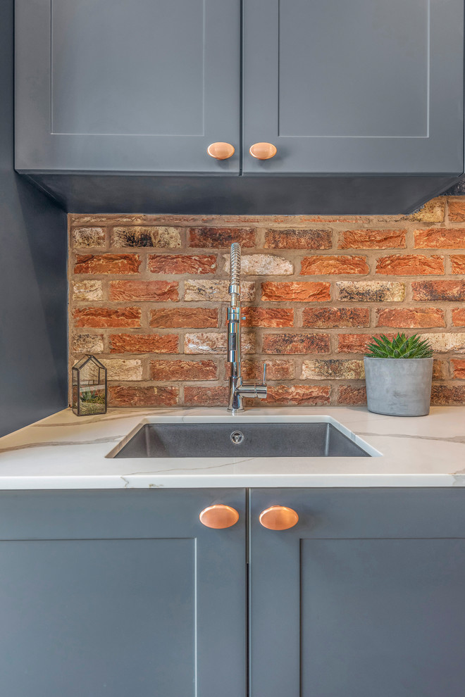 Design ideas for an industrial single-wall kitchen in Berkshire with shaker cabinets, blue cabinets, brick splashback, black appliances, with island and brown floor.