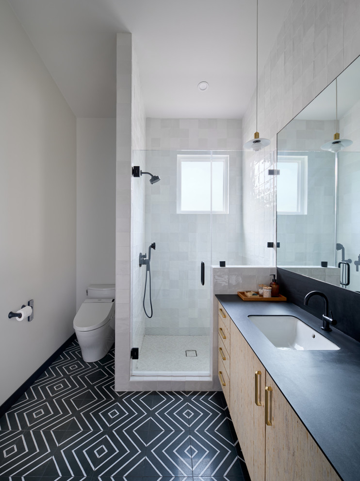 This is an example of a mid-sized modern master bathroom in Los Angeles with flat-panel cabinets, light wood cabinets, a corner shower, a bidet, white tile, ceramic tile, white walls, porcelain floors, an undermount sink, solid surface benchtops, multi-coloured floor, a hinged shower door, black benchtops, a single vanity, a floating vanity and vaulted.