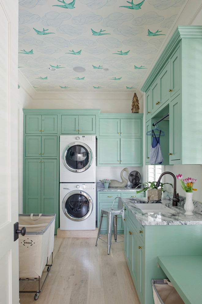 Design ideas for a transitional dedicated laundry room in Atlanta with a double-bowl sink, shaker cabinets, light hardwood floors, a stacked washer and dryer and blue cabinets.
